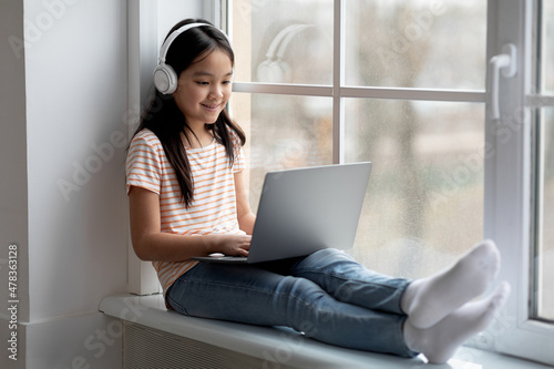 Cheerful little korean girl with wireless headset using laptop