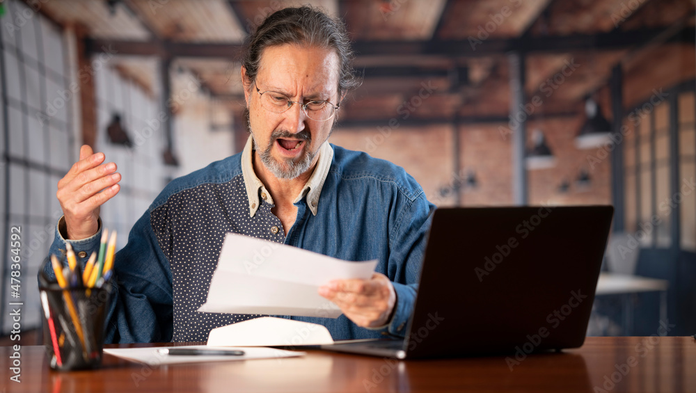 Angry stressed businessman opening envelope reading bad news in mail letter. Mad man feels frustrated about high bills, dismissal notice, bank debt, tax invoice or mistake sits at home office desk. Angry stressed businessman opening envelope reading bad news in mail letter. Mad man feels frustrated about high bills, dismissal notice, bank debt, tax invoice or mistake sits at home office desk.