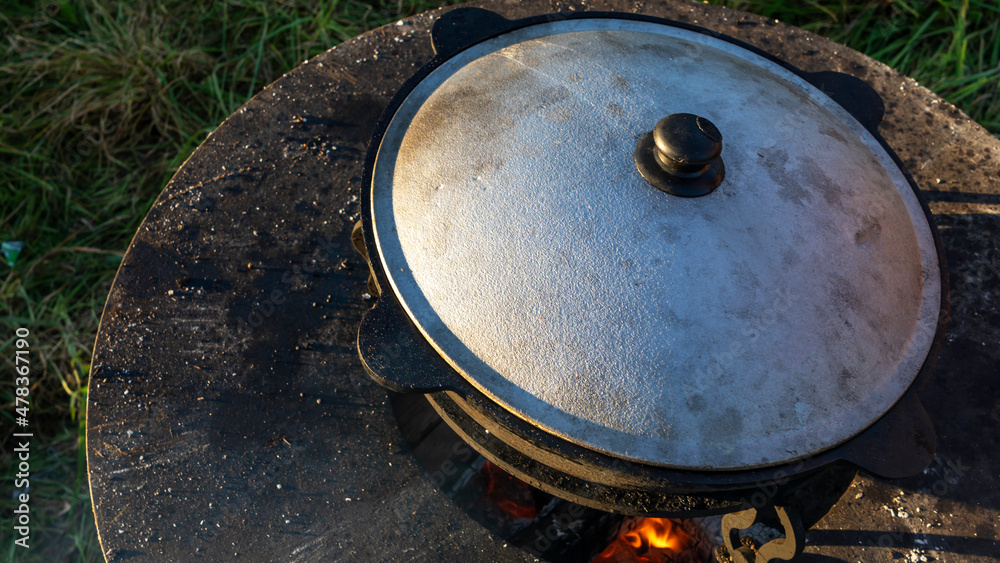 Big pot with street food preparing on fire outdoors. Kitchen outdoors. Metal cauldron on the fire. Big pot with street food preparing on fire outdoors. Kitchen outdoors. Metal cauldron on the fire.
