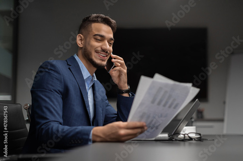 Happy arab CEO reading documents and having phone conversation