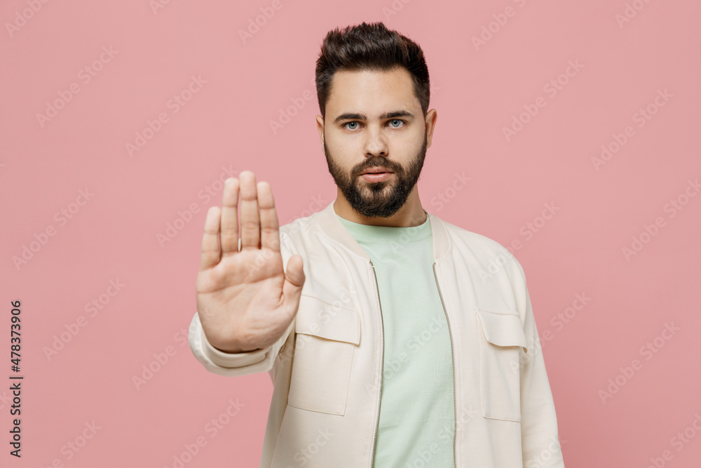 Young strict serious european sad caucasian man 20s wearing trendy jacket shirt showing stop gesture with palm isolated on plain pastel light pink background studio portrait. People lifestyle concept. Young strict serious european sad caucasian man 20s wearing trendy jacket shirt showing stop gesture with palm isolated on plain pastel light pink background studio portrait. People lifestyle concept.
