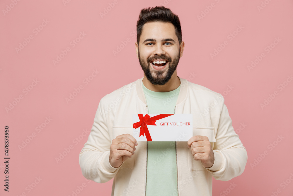 Young smiling happy man 20s wearing trendy jacket shirt hold gift certificate coupon voucher card for store isolated on plain pastel light pink background studio portrait. People lifestyle concept