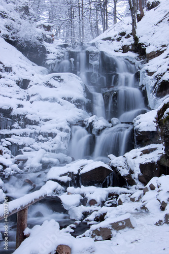 The waterfall is covered with snow. Winter landscape by the river. © malshak_off