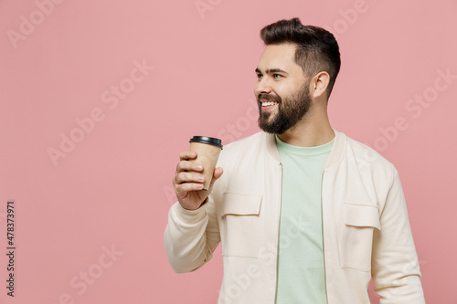 Young smiling happy man 20s in trendy jacket shirt hold takeaway delivery craft paper brown cup coffee to go isolated on plain pastel light pink background studio portrait. People lifestyle concept. © ViDi Studio