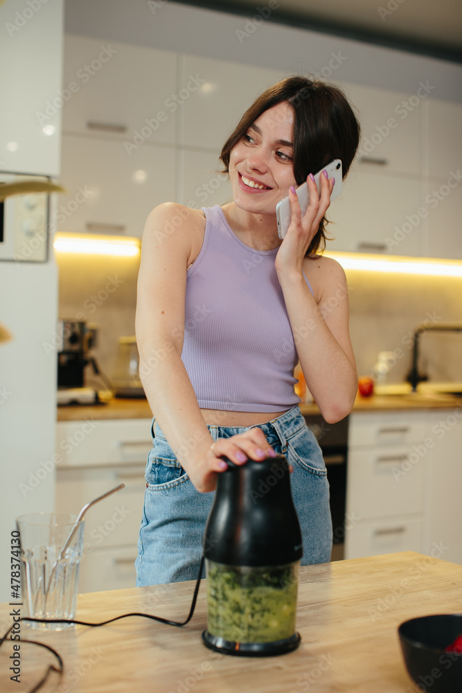 Happy young slim girl making fresh organic smoothie using blender in the kitchen. Happy young slim girl making fresh organic smoothie using blender in the kitchen.