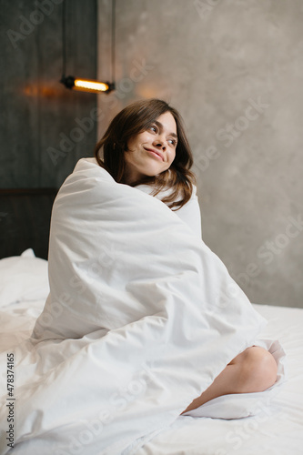 Beautiful young woman wrapped with soft blanket on bed after awakening.