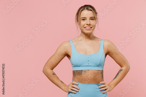 Young strong sporty athletic fitness trainer instructor woman wear blue tracksuit spend time in home gym hold arms on waist isolated on pastel plain pink background. Workout sport motivation concept.