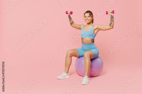 Full size young strong sporty athletic fitness trainer instructor woman wear blue tracksuit spend time in home gym sit on fitball isolated on pastel plain light pink background. Workout sport concept.