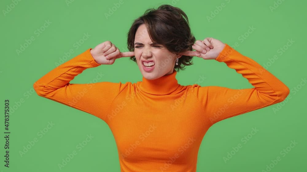 Displeased angry young brunette woman 20s wears orange shirt closed eyes cover ears do not want to listen scream isolated on plain green background studio portrait. People emotions lifestyle concept Displeased angry young brunette woman 20s wears orange shirt closed eyes cover ears do not want to listen scream isolated on plain green background studio portrait. People emotions lifestyle concept