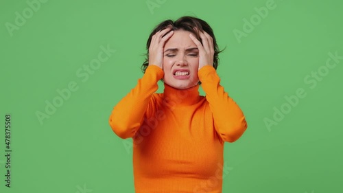 Upset worried disturb displeased young brunette woman 20s years old wears orange shirt sigh suspire sithe put hands on face say what why how no way isolated on plain green background studio portrait photo