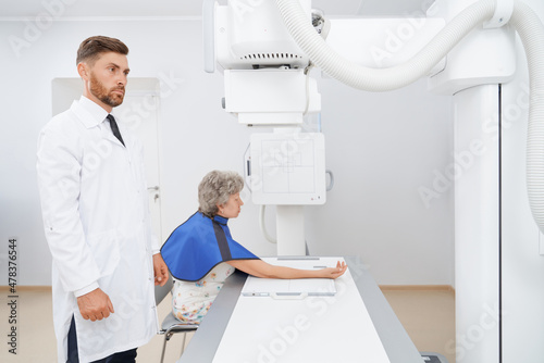 Side view of doctor radiologist at cabinet of ultra diagnostic seriously looking at screen . Professional doing use with big modern tool above hand of patient. Concept of medicine.