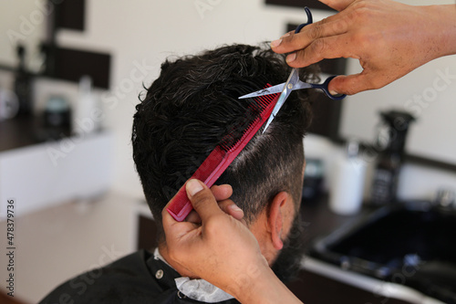 Barber hands with scissors cutting man's hair