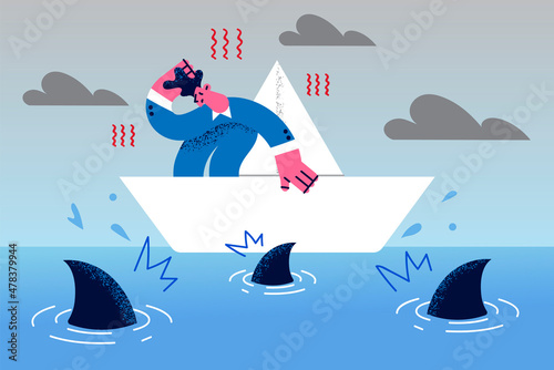 Businessman on paper boat surrounded by sharks 