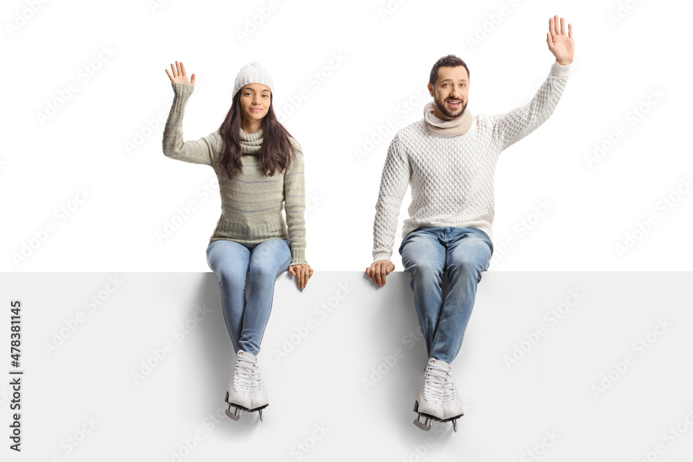 Fototapeta premium Young man and woman with ice skates sitting on a blank panel and waving
