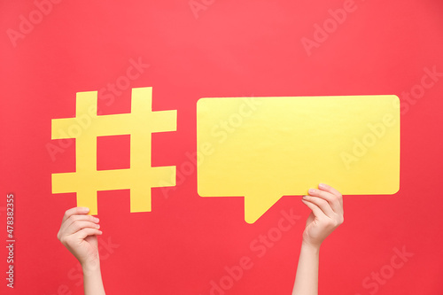 Female hands holding yellow paper hashtag symbol and speech bubble, hash sign of famous media content, isolated on red color background. Post viral web network, blogging blog website strategy concept