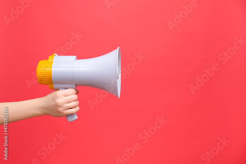 Close up of female hand holding bullhorn public address megaphone, Hot news, announce discounts sale, hurry up, isolated on red background wall with copy space for advertisement. Communication concept