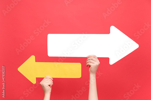 Close up of female hands holding two paper arrow pointing left and right, isolated on red color background studio with copy space for your text or design. Business vision, choice, achievement concept photo