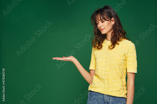 Pretty young girl holding blank copy space aside on palm, show advertising place with sale offer on green background