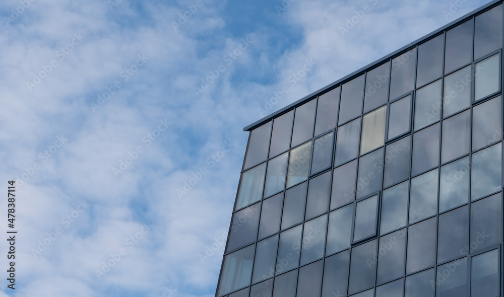 Photo of a building with glass windows in the city against a blue sky with white clouds