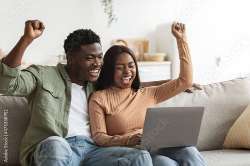 Fotografie, Obraz Lucky black couple trading together on Internet, home interior