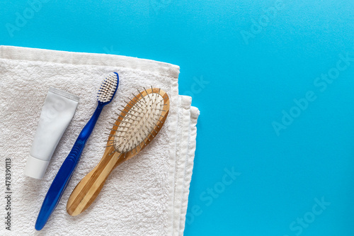 Flatlay of white towel, hair brush, and toothbrush in a box with a blue background and copy space for your text. Morning routine during travel