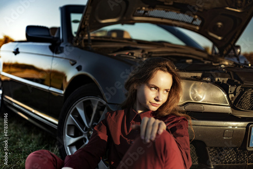 A beautiful girl near a car broken down in a field, a retro convertible