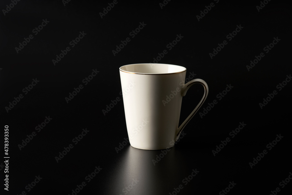A white mug with a golden rim on top and a stripe on the handle on a black background. Copy space. A white mug with a golden rim on top and a stripe on the handle on a black background. Copy space.