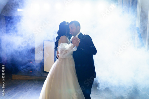Canvas the bride and groom in wedding dresses dance in a dark hall in heavy smoke