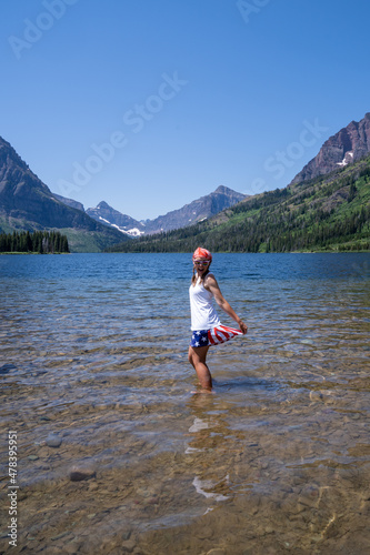 Cute woman wearing patriotic America USA gear stands in Two Medicine Lake in Glacier National Park © MelissaMN