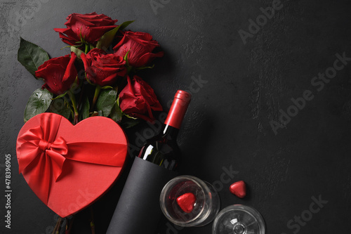 Fototapeta Naklejka Na Ścianę i Meble -  Valentine's day gift, red wine, bouquet of roses on black background. Greeting card with copy space. View from above.