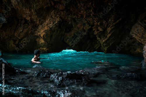 young man looking at light in pool inside dark natural cave