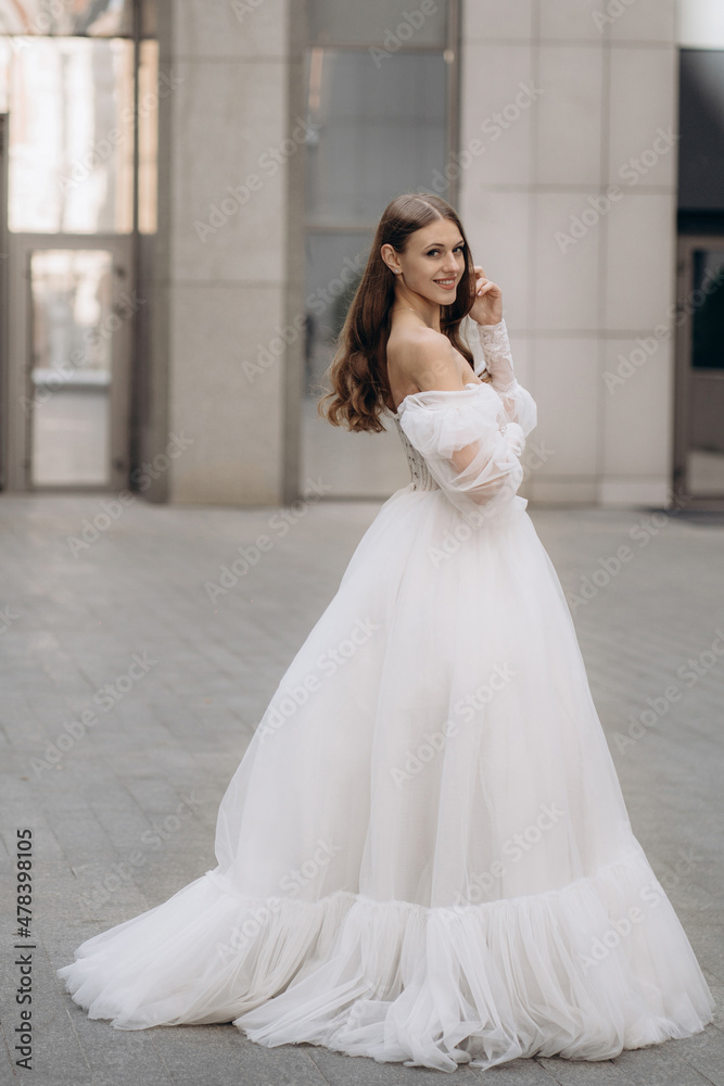Full length portrait of beautiful bride with long curly hair in white wedding dress. Fashionable long sleeves white wedding dress with bare shoulders, beads, lace, and neckline. Adorable bride Full length portrait of beautiful bride with long curly hair in white wedding dress. Fashionable long sleeves white wedding dress with bare shoulders, beads, lace, and neckline. Adorable bride