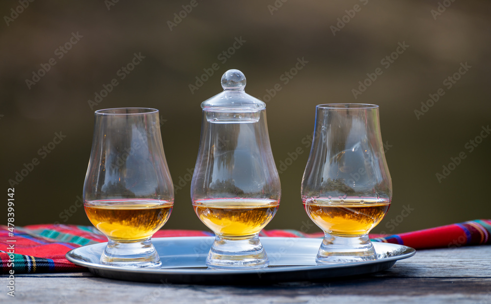 Tasting glasses of scotch whisky strong drink and red Scottisch tartan on old outdoor table Tasting glasses of scotch whisky strong drink and red Scottisch tartan on old outdoor table