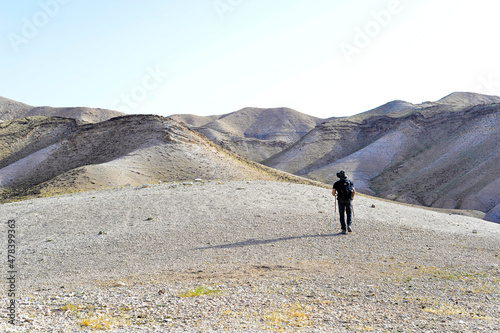 Group of tourists hiking, travelers on a trail in an Israeli desert mountains. Backpackers tourists group walking hiking rocks desert path trail. Israel desert hills landscape at spring, green grass