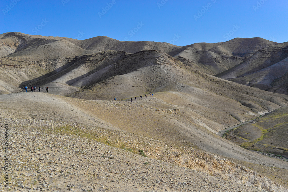 Group of tourists hiking, travelers on a trail in an Israeli desert mountains. Backpackers tourists group walking hiking rocks desert path trail. Israel desert hills landscape at spring, green grass Group of tourists hiking, travelers on a trail in an Israeli desert mountains. Backpackers tourists group walking hiking rocks desert path trail. Israel desert hills landscape at spring, green grass