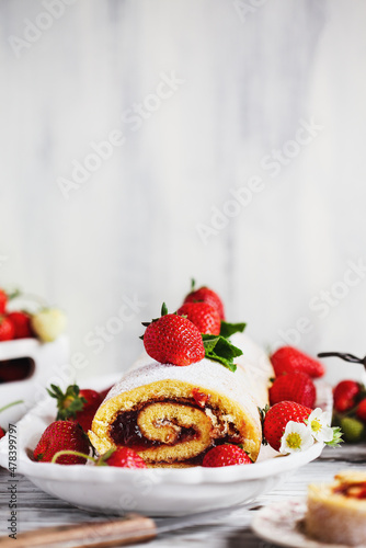Homemade strawberry shortcake cake roll, Sponge or Roulade with a berry jam filling with powdered sugar. Dessert over a white rustic wood table. Selective focus with blurred foreground and background.