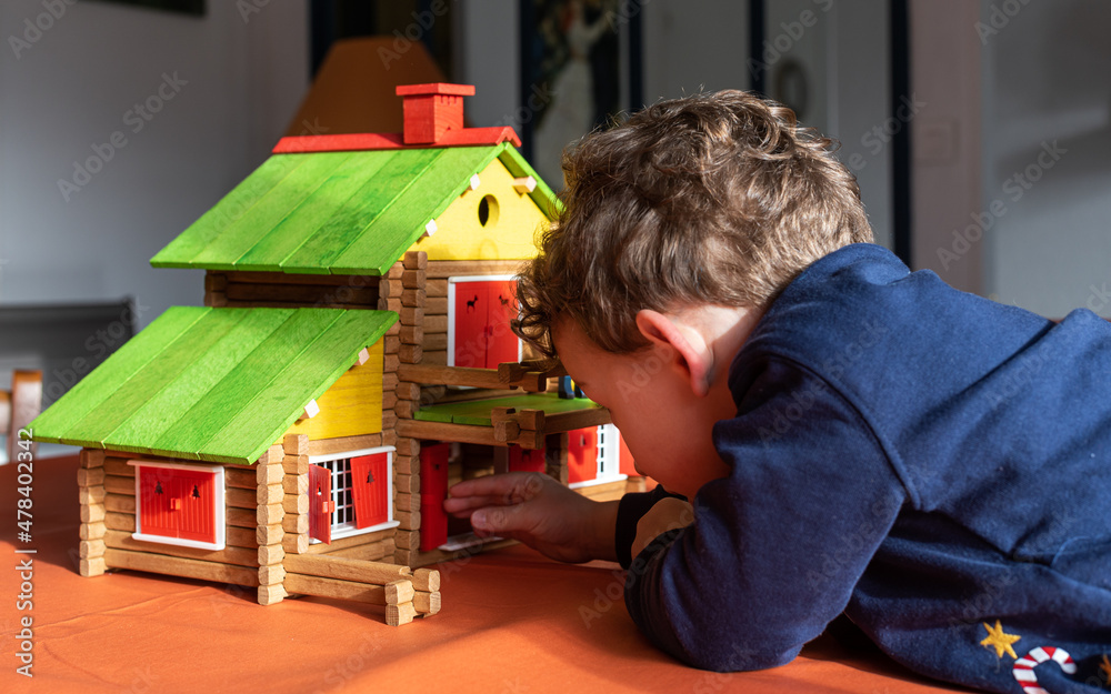 Obraz premium Caucasian child boy playing with a vintage wooden log cabin on a table, a creative wood construction toy.