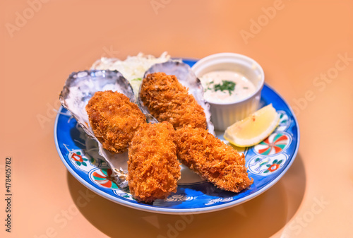 Japanese shellfish dish of battered and deep fried oysters made by adding egg whites and bread crumbs called kaki-furai or kaki fry served in their shell with a sauce and a lemon slice in a plate. photo