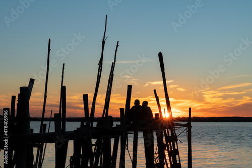 couple of men sitting watching the sunset in the stilt port of Carrasqueira, in Comporta, Portugal