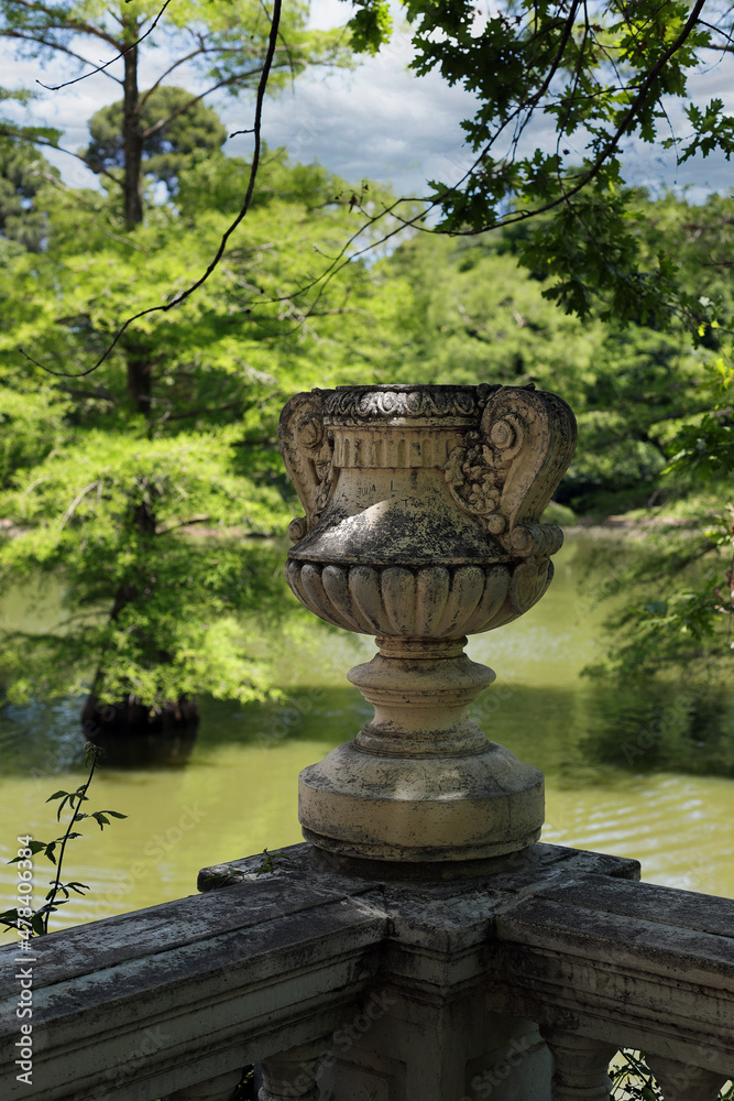 Escultura de jarrón de piedra estilo clásico en parque con lago y arboles Escultura de jarrón de piedra estilo clásico en parque con lago y arboles