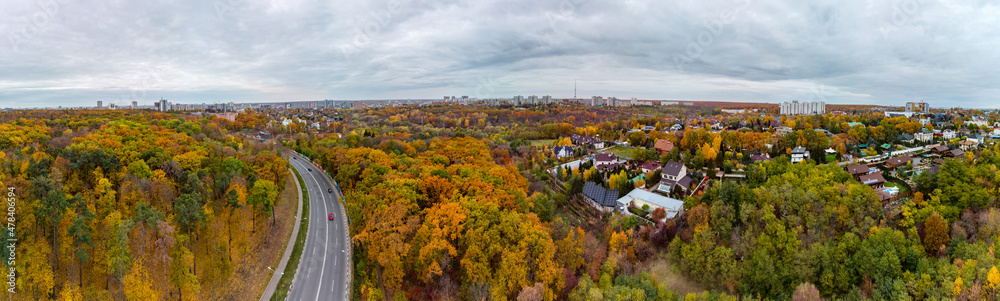 Aerial wide panorama of scenic road in autumnal residential district. Fly above street in autumn city park with cloudy epic sky. Treetop view on Kharkiv, Ukraine