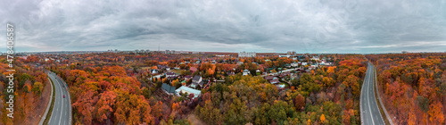 Aerial wide colorful panorama of scenic road in autumnal residential district. Fly above autumn city park with cloudy epic sky. Treetop view on Kharkiv, Ukraine