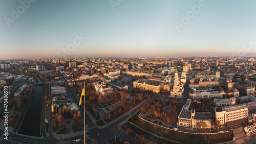 Flagpole with flag of Ukraine with epic sunny autumn cityscape. Panoramic aerial view above river Lopan embankment near Dormition Cathedral in Kharkiv, Ukraine