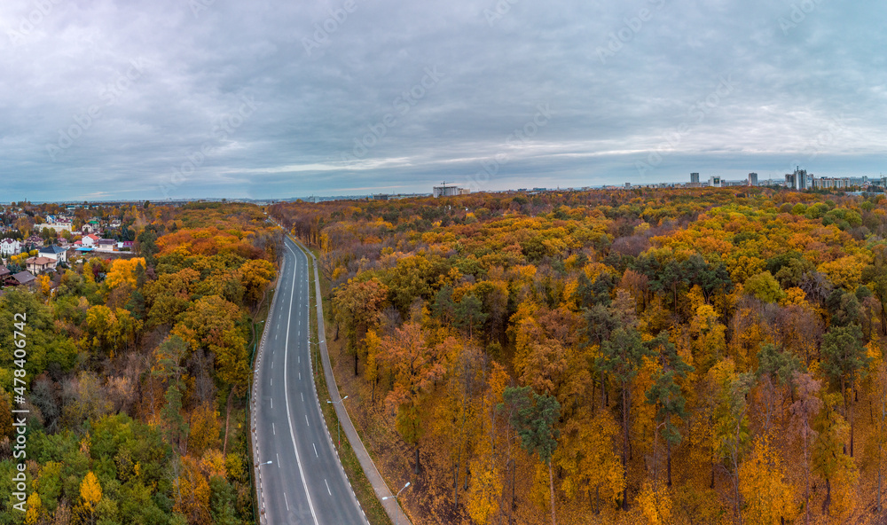 Aerial scenic road panorama in autumnal residential district. Fly above street in autumn city park with cloudy epic sky. Treetop view on Kharkiv, Ukraine