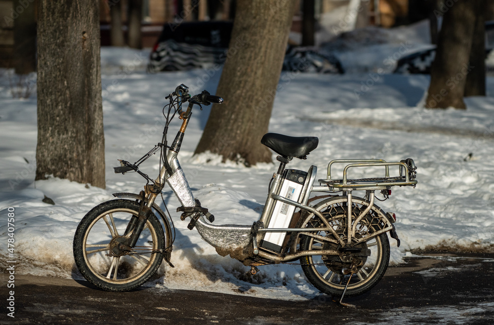 Fototapeta premium Old broken electric bike on the sidewalk in winter.