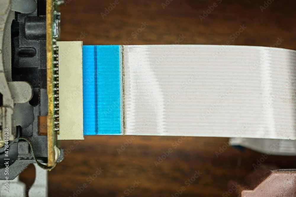 part of a disassembled electronic device with parts board and white blue long plastic ribbon