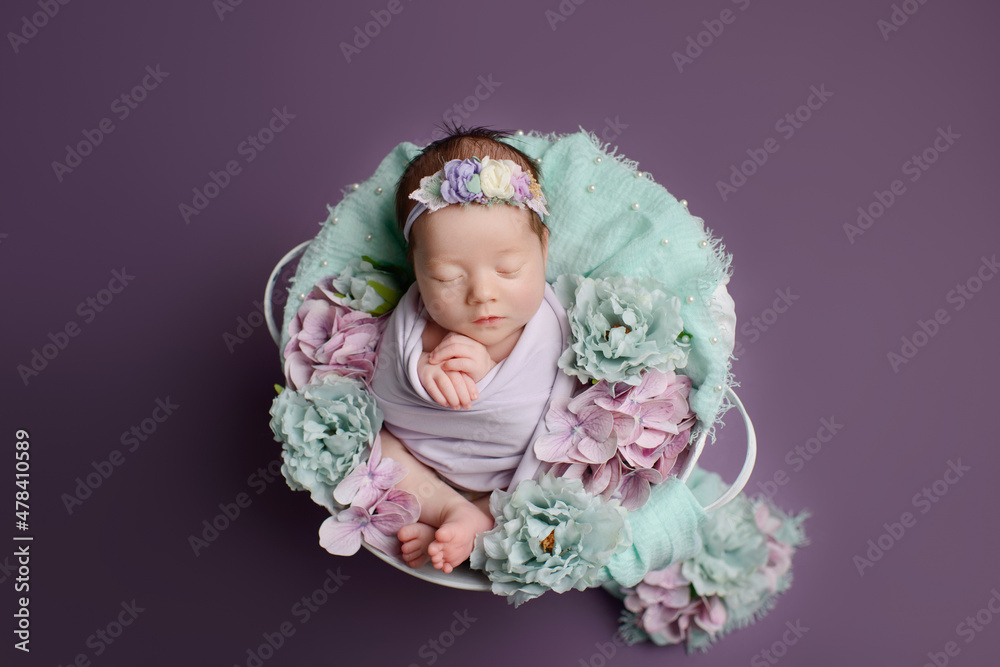 Fototapeta premium Newborn girl on a purple background. Photoshoot for the newborn. A portrait of a beautiful sleeping newborn baby girl