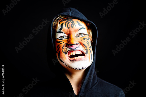 Portrait of a boy with strange and scary gesture, made up with tiger face, isolated on black background Fotobehang