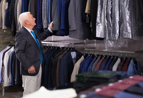 Positive mature customer looking jacket in men clothes store