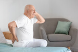 Senior man suffering from back pain on bed at home